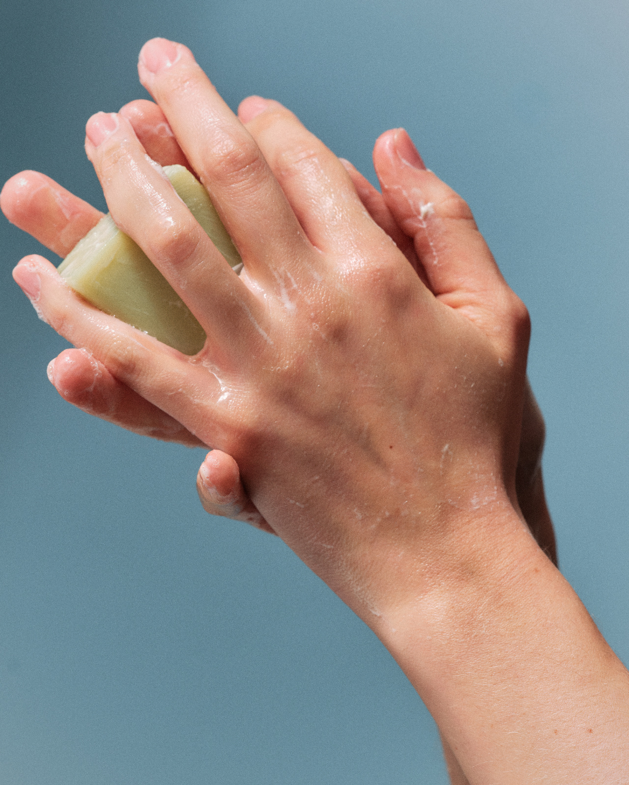 Hands lathering a bar of soap against a blue background, handwashing between clients